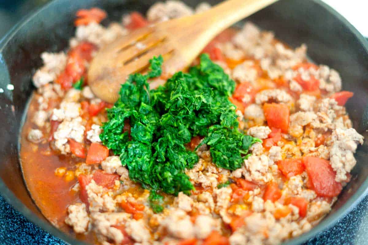 Making the filling for stuffed shells with pork sausage, spinach, tomatoes, garlic and ricotta cheese.