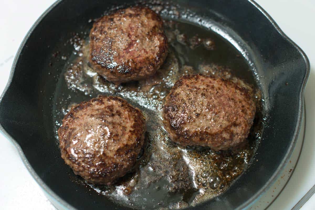Hamburgers cooking in a Cast Iron Skillet