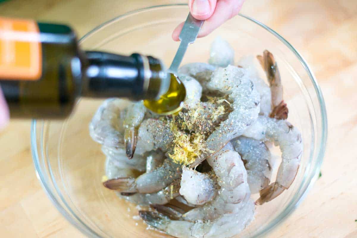 Tossing shrimp with salt, pepper, lemon zest, and olive oil.