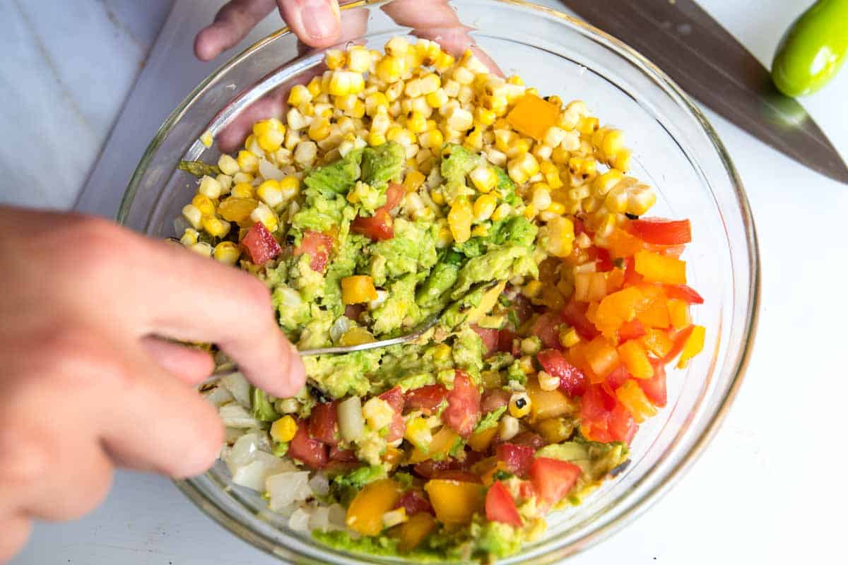 Using a fork to mash grilled avocados with the other ingredients