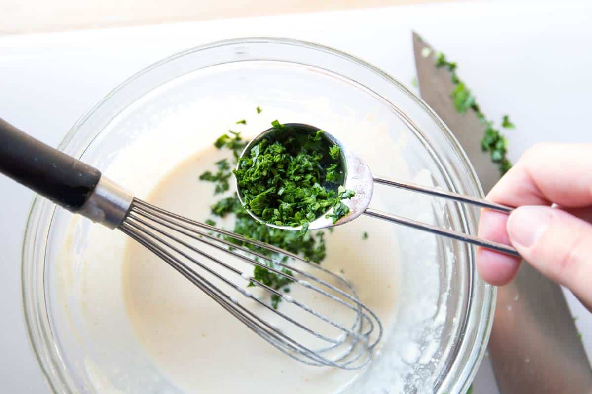 Adding parsley to tahini sauce mixture