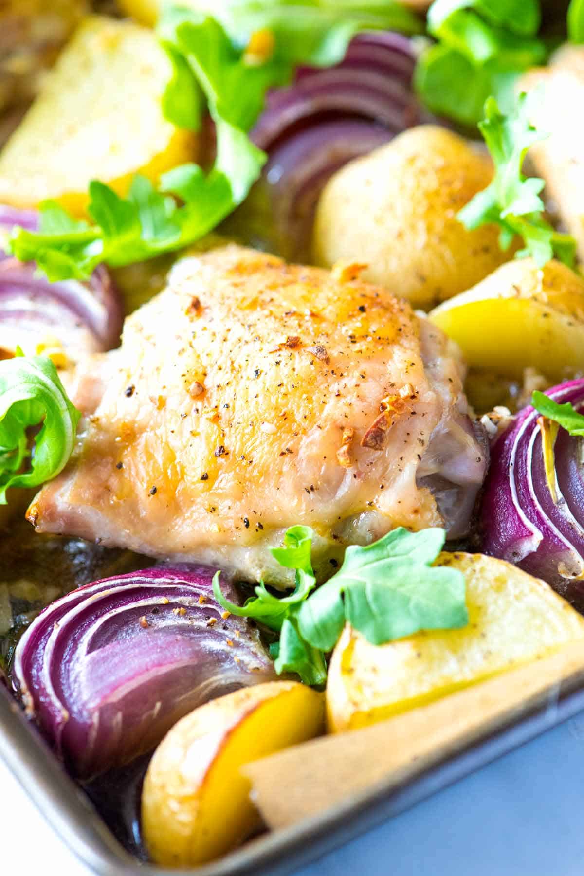 Crispy baked chicken thighs on a sheet pan with potatoes and onions