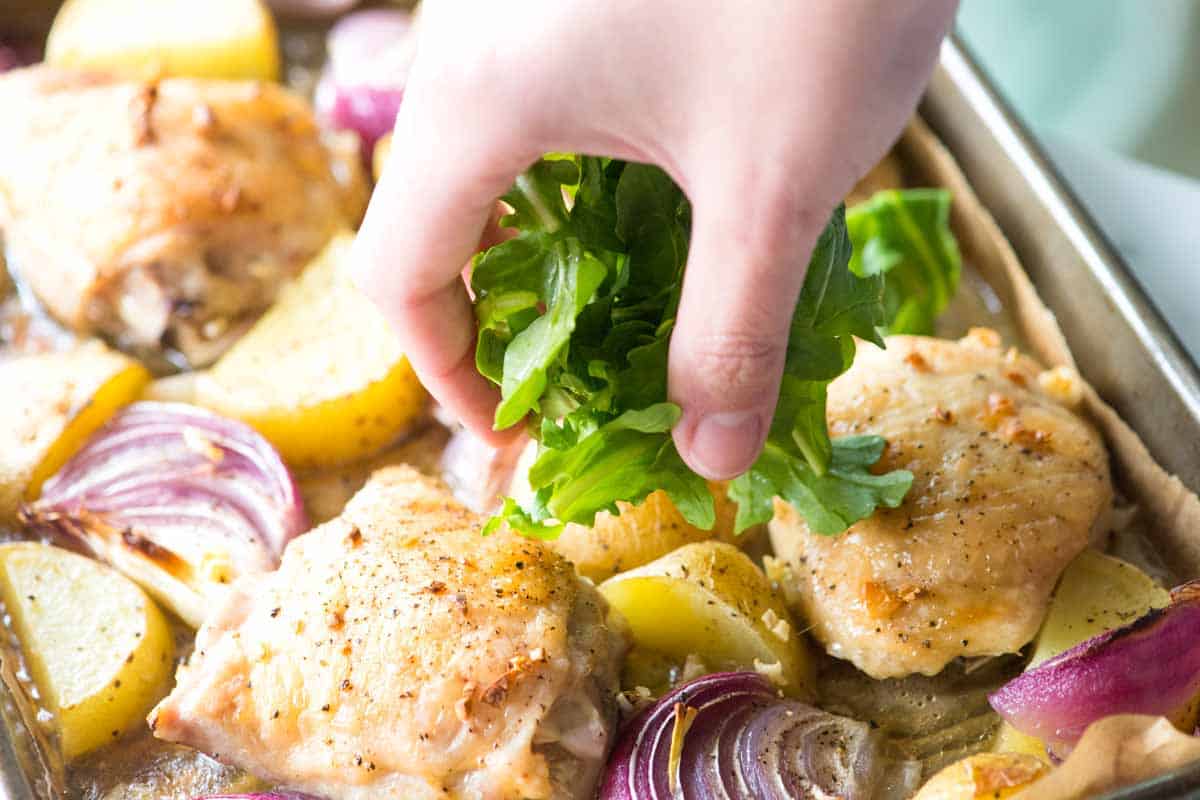 Adding baby arugula to the sheet pan of baked chicken and potatoes