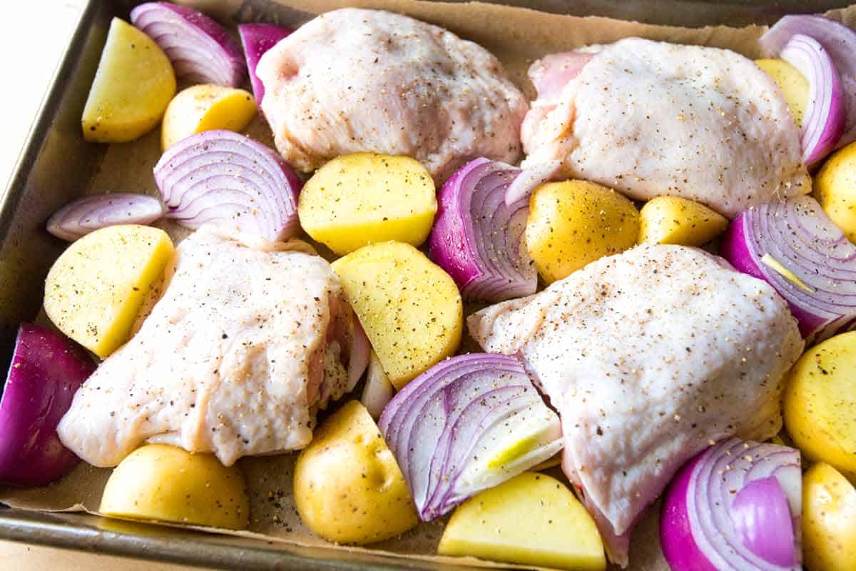 Baking chicken thighs, potatoes, and onions on a sheet pan