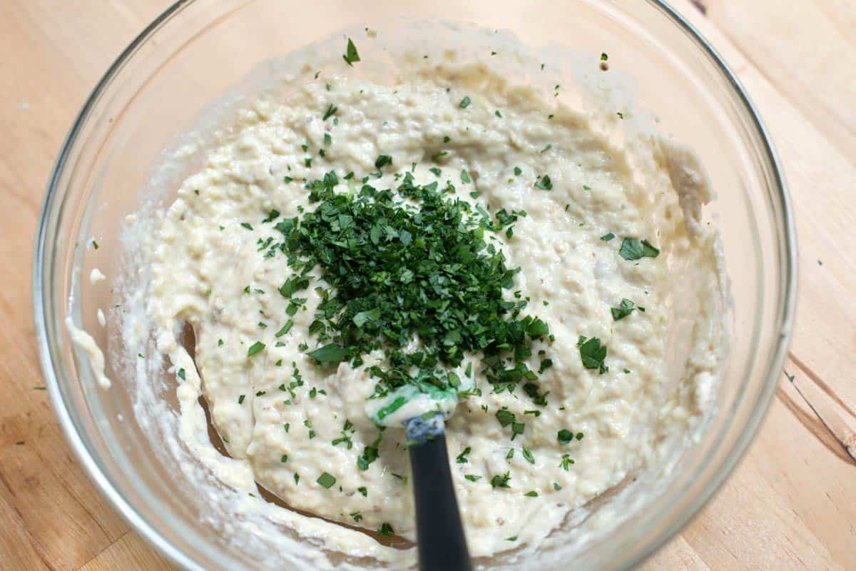 Mashing the roasted eggplant into a flavorful mixture of tahini, lemon juice, and spices with a fork.