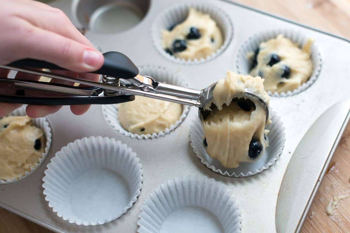 Scooping blueberry muffin batter into  muffin pan