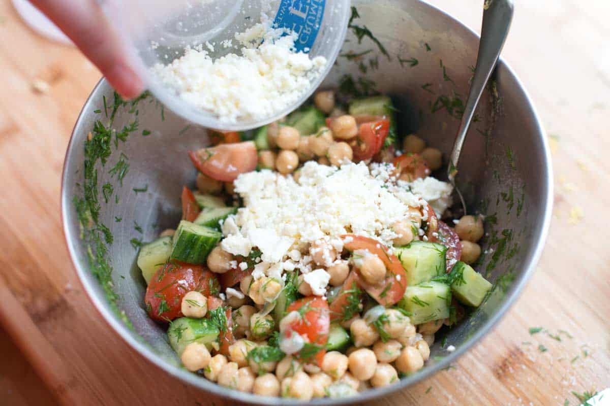 Adding feta to chickpeas, cucumbers and tomatoes.