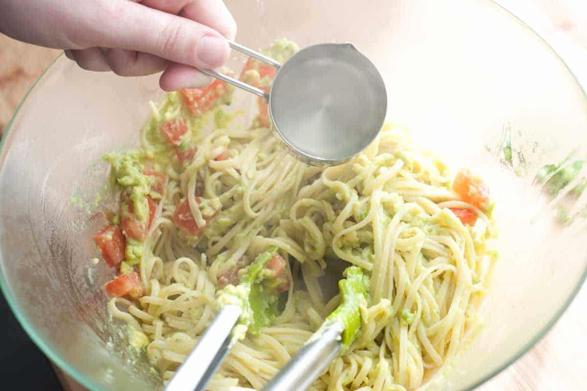 Tossing the avocado sauce and pasta together in a bowl