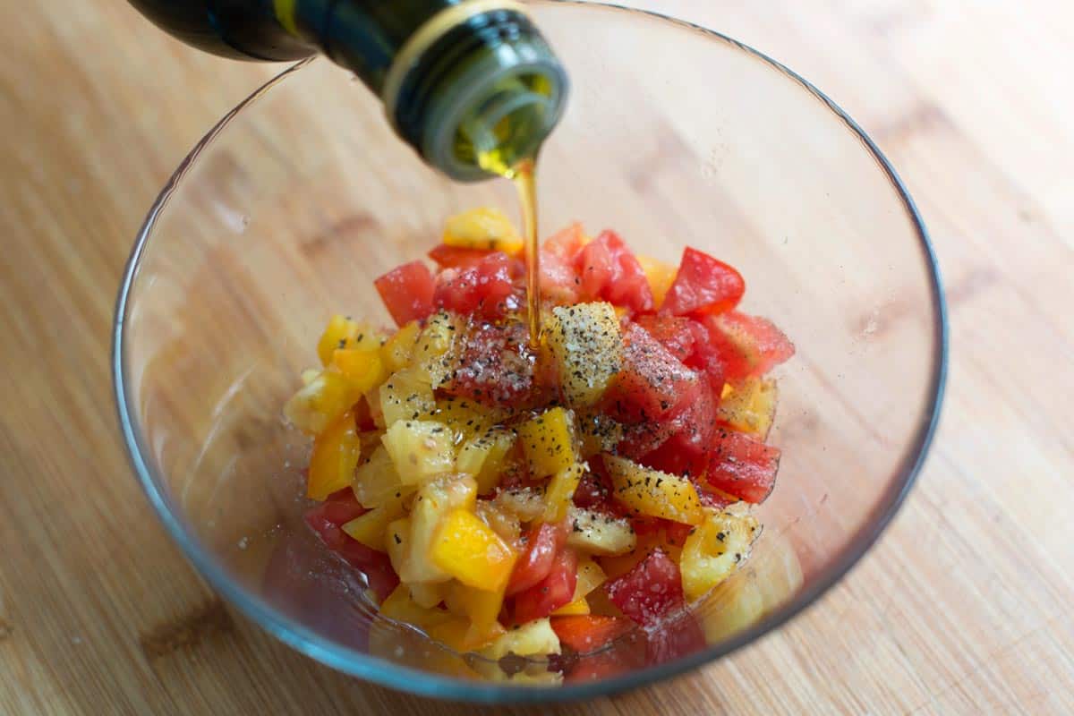 Adding olive oil, salt and pepper to chopped fresh tomatoes for the bruschetta topping