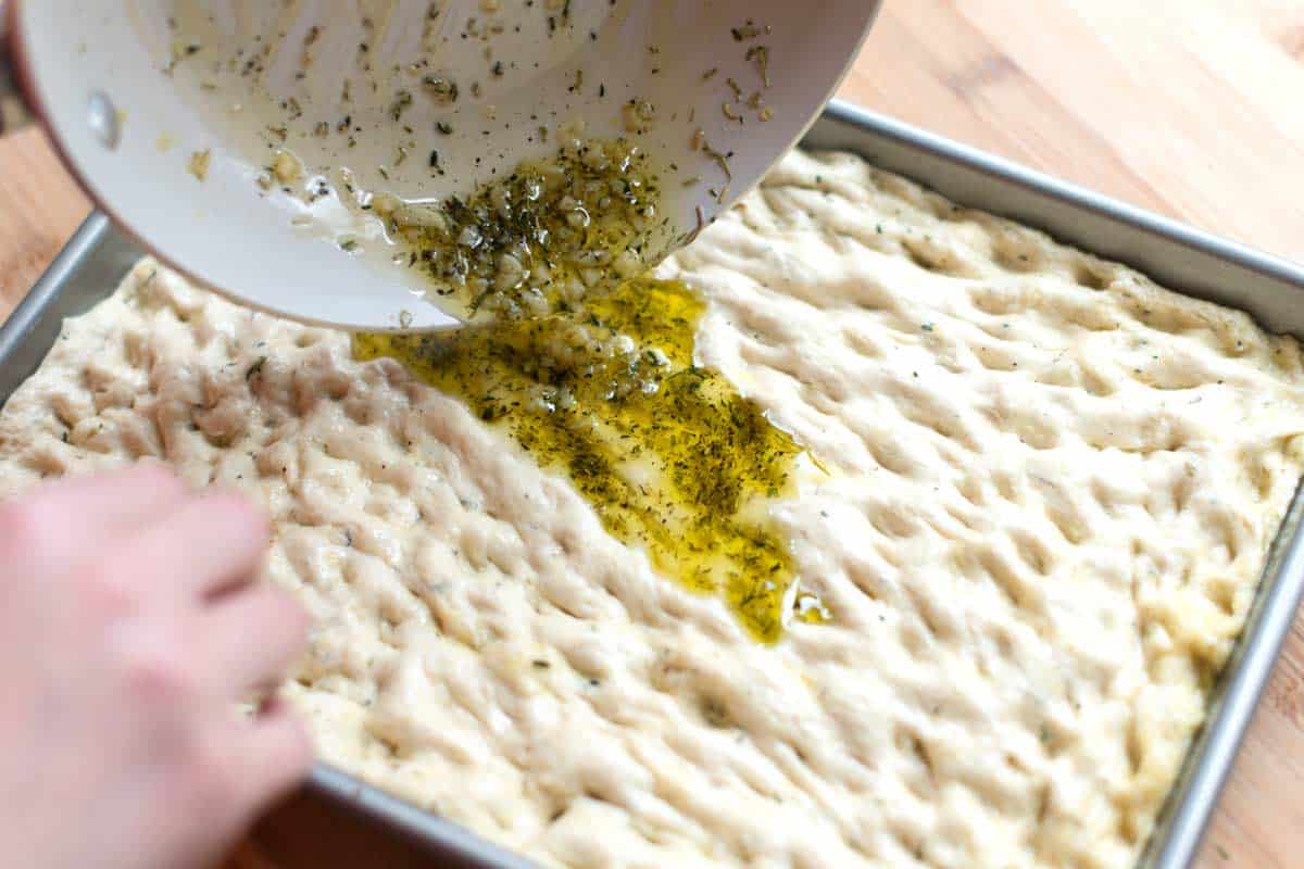 Adding the infused olive oil, garlic, and herbs to focaccia dough