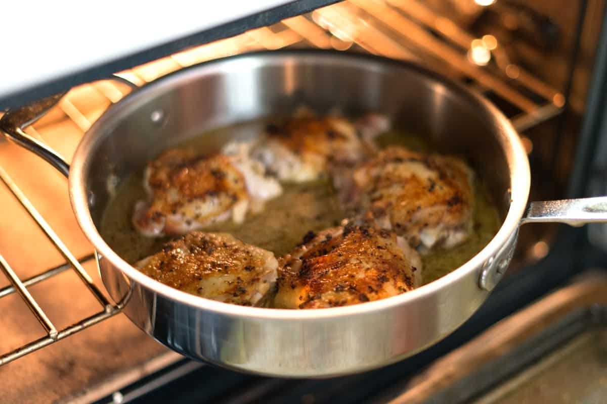 Placing a  pan of lemon chicken thighs into the oven to finish cooking (there is lemon juice and chicken stock in the pan also, which keeps the chicken thighs super moist and tender).