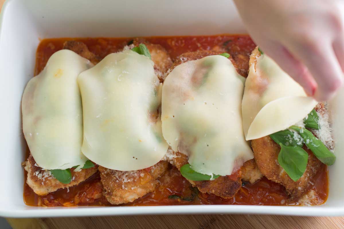Adding parmesan cheese and provolone cheese to chicken parmesan.