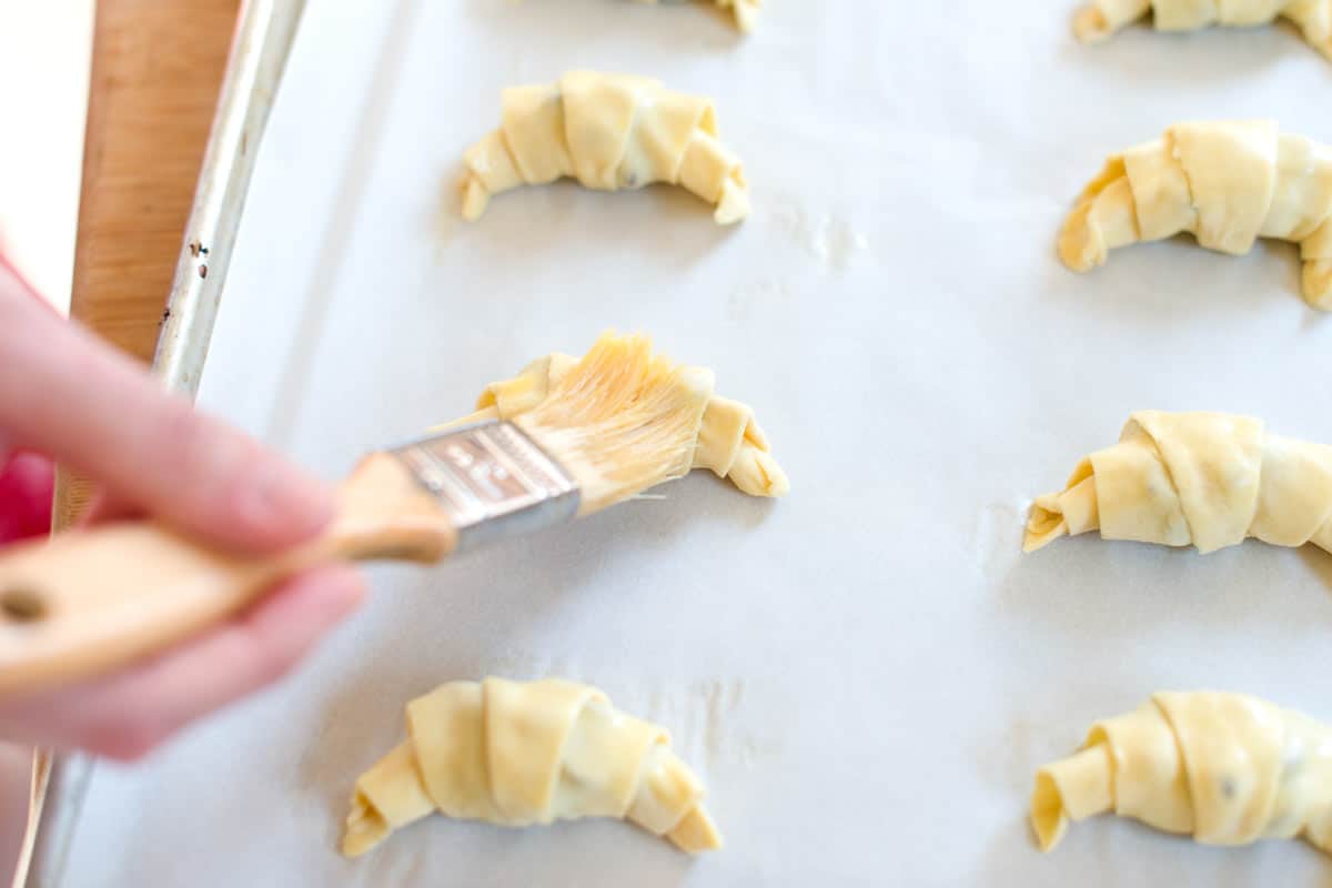 Brushing egg wash over unbaked chocolate croissants before baking them.