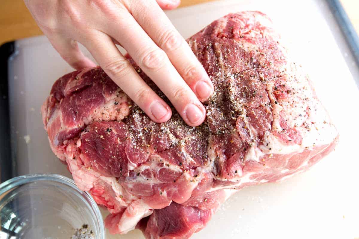 Seasoning pork shoulder with salt and pepper before adding to the slow cooker.