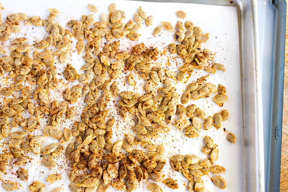 Spiced pumpkin seeds spread out onto a baking sheet.