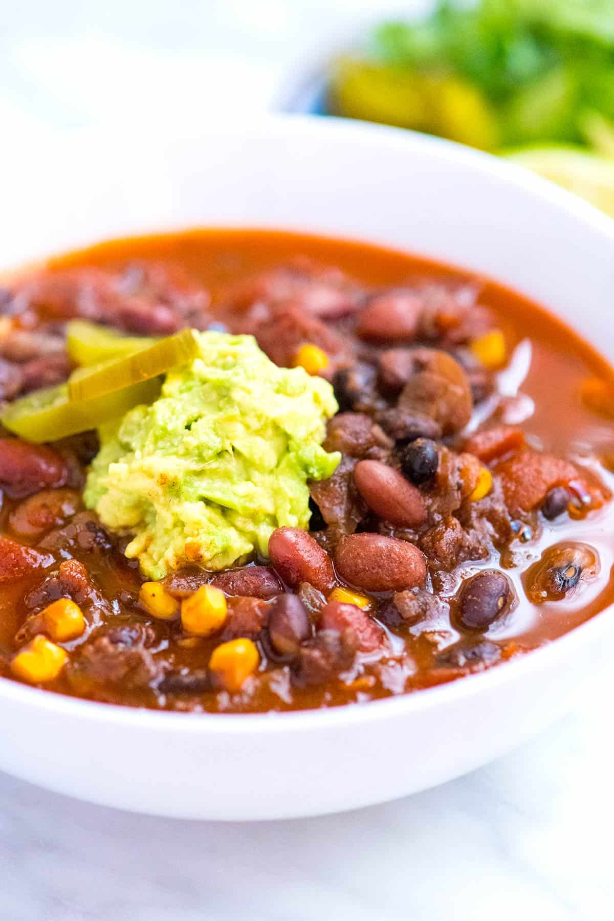 Bowl of vegetarian bean chili with avocado on top.