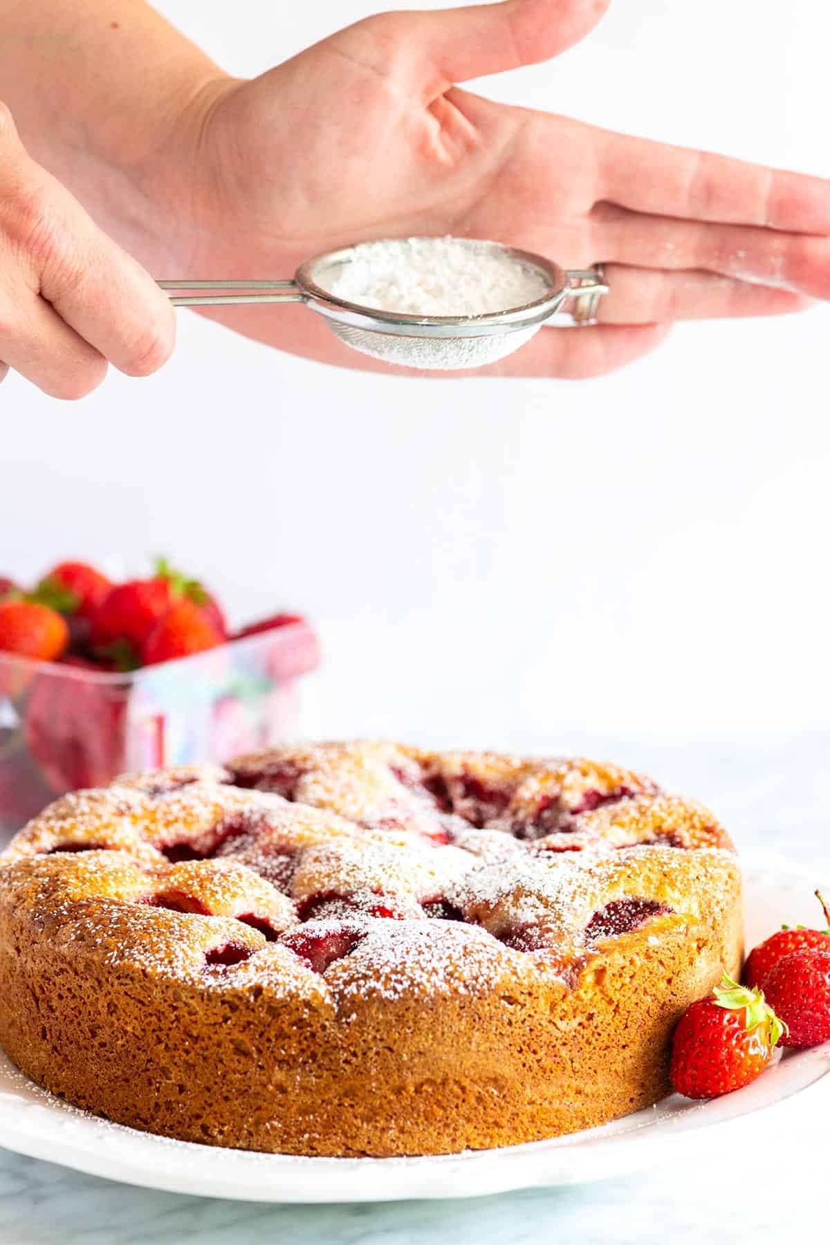Stunning fresh strawberry cake recipe that’s extremely simple to make. The batter is made in one bowl! So easy. Homemade Strawberry Cake with powdered sugar on top