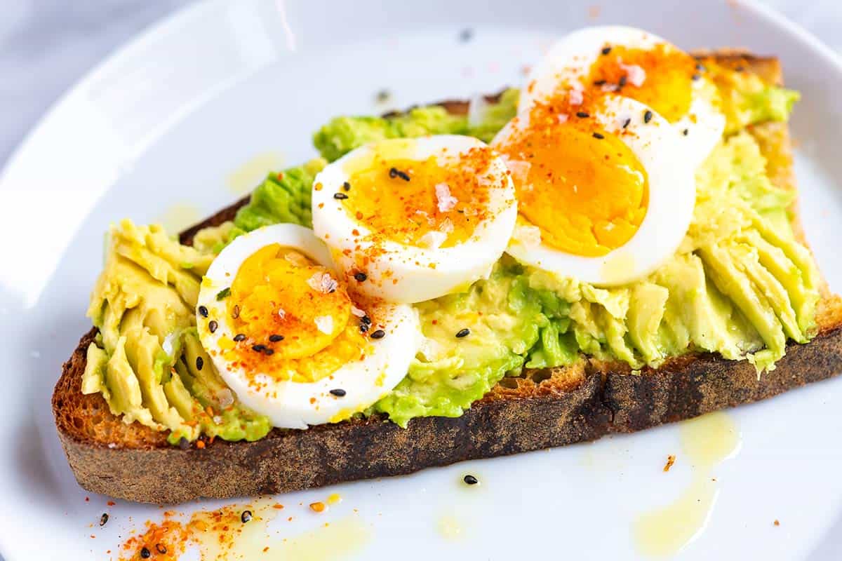 Closeup of fresh made avocado toast with slice hard-boiled egg, seasonings, and flaky salt