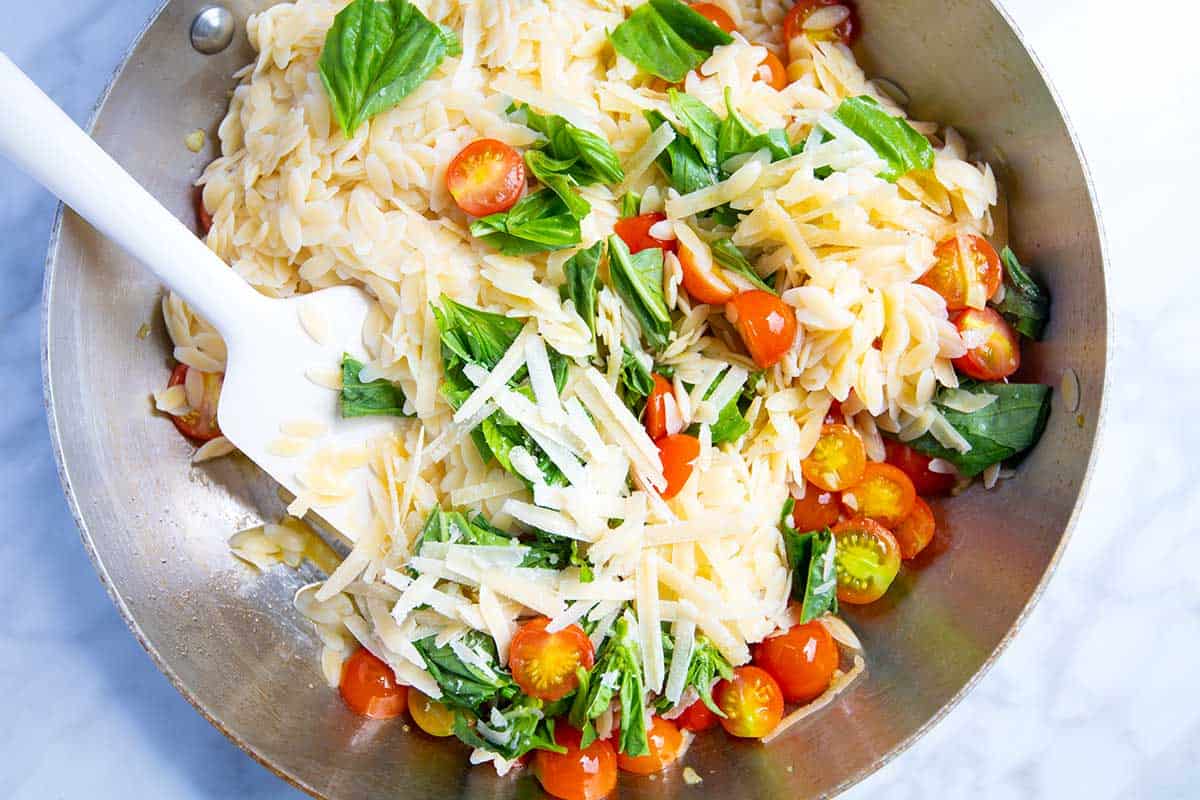 Stirring orzo pasta with fresh tomatoes, basil and parmesan.