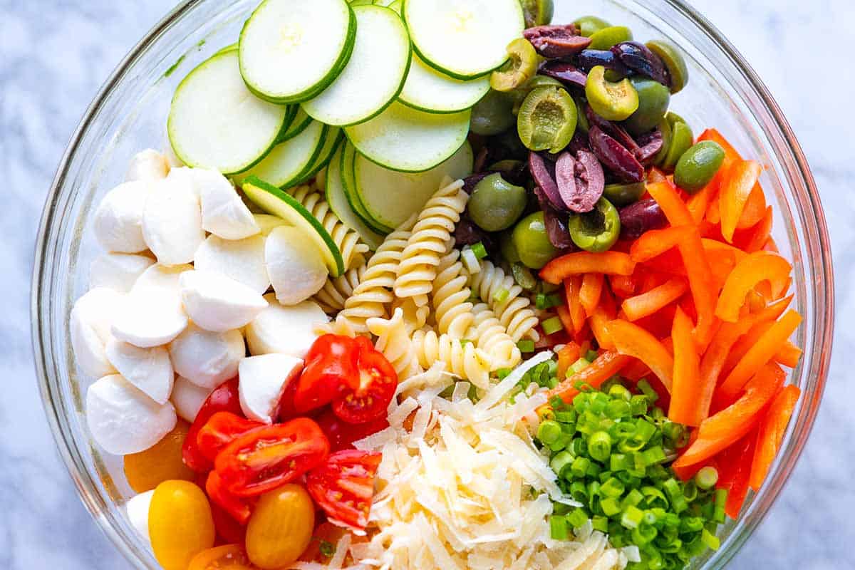 Pasta salad ingredients in a bowl (pasta, tomatoes, olives, cheese, red bell pepper)