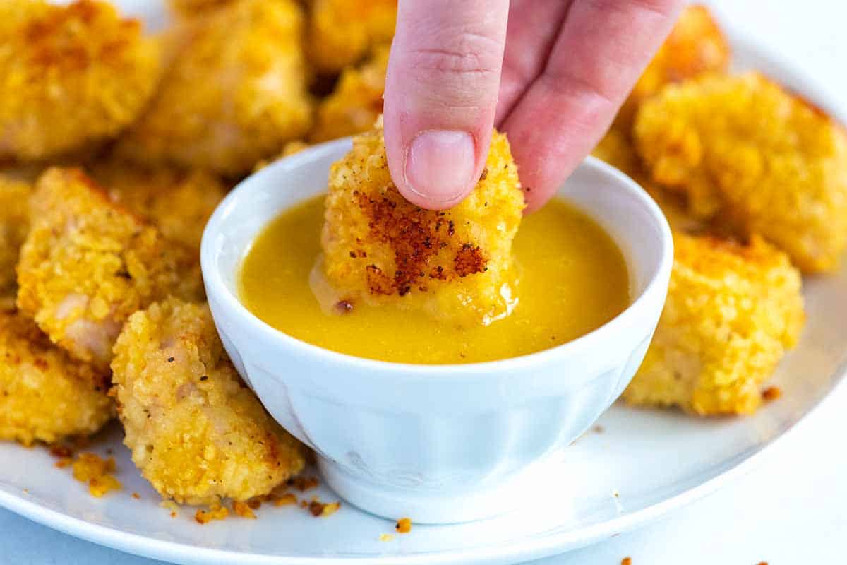 Homemade chicken nuggets being dipped in honey mustard