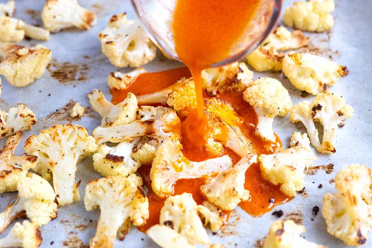 How to Make Buffalo Cauliflower Wings: Pouring buffalo sauce over roasted cauliflower