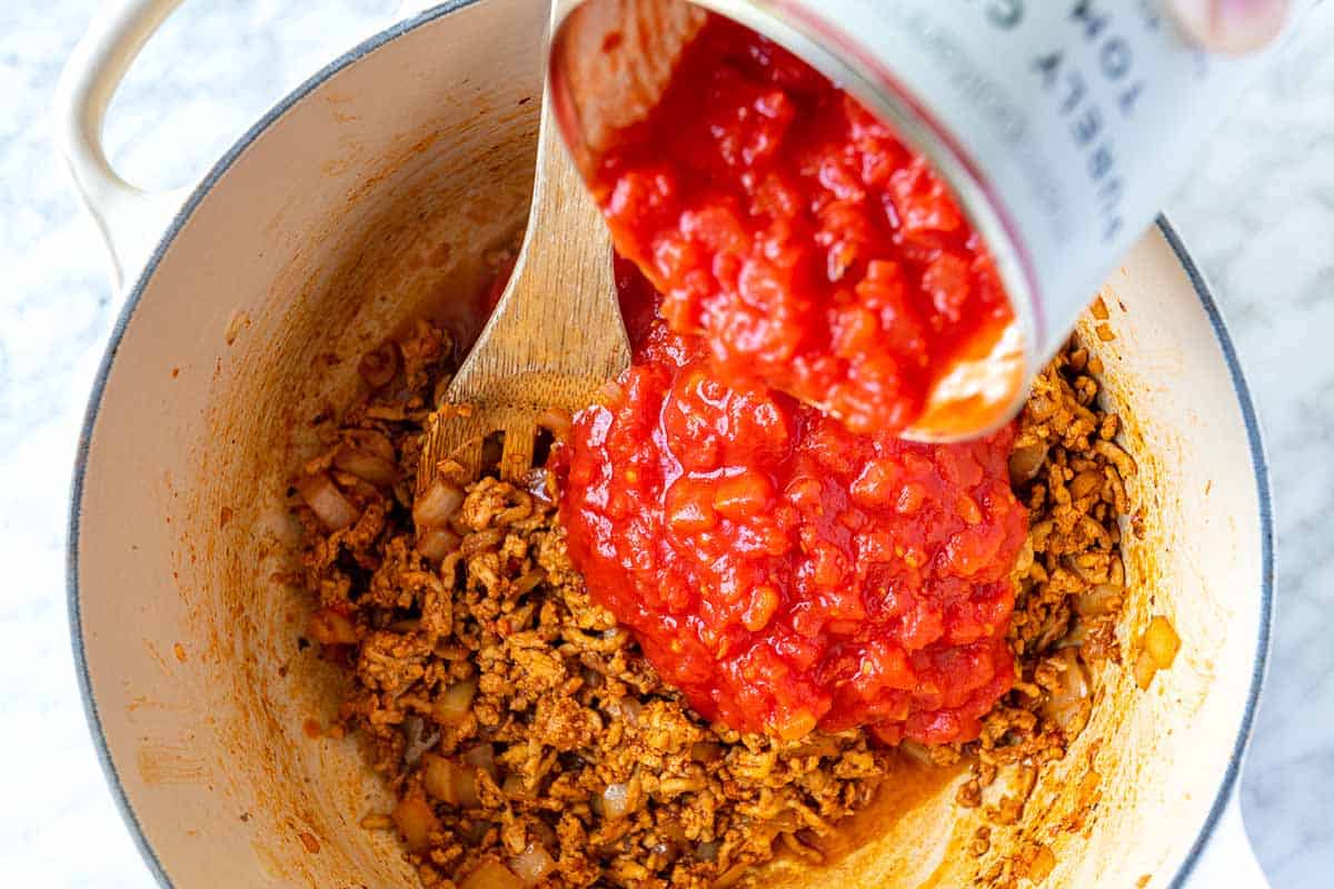 Adding tomatoes to the pot with browned meat