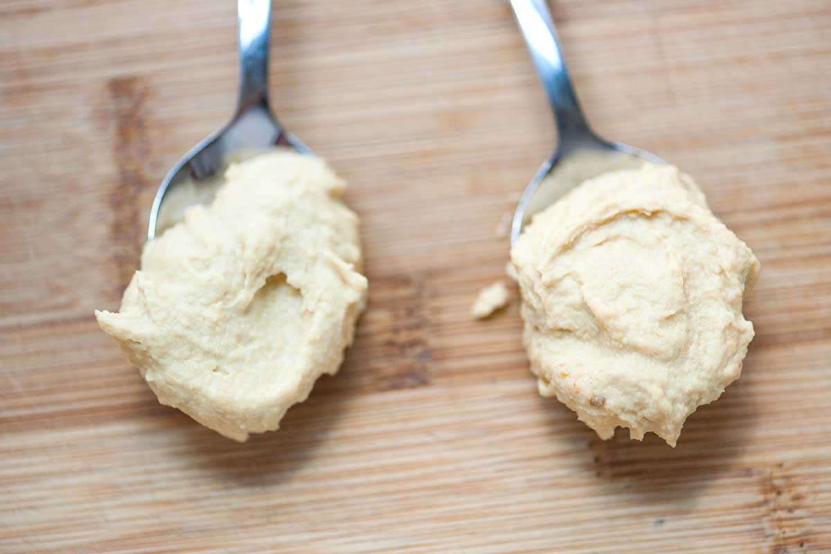 A photo showing the comparison of hummus made with peeled chickpeas and hummus made with skin-on chickpeas.