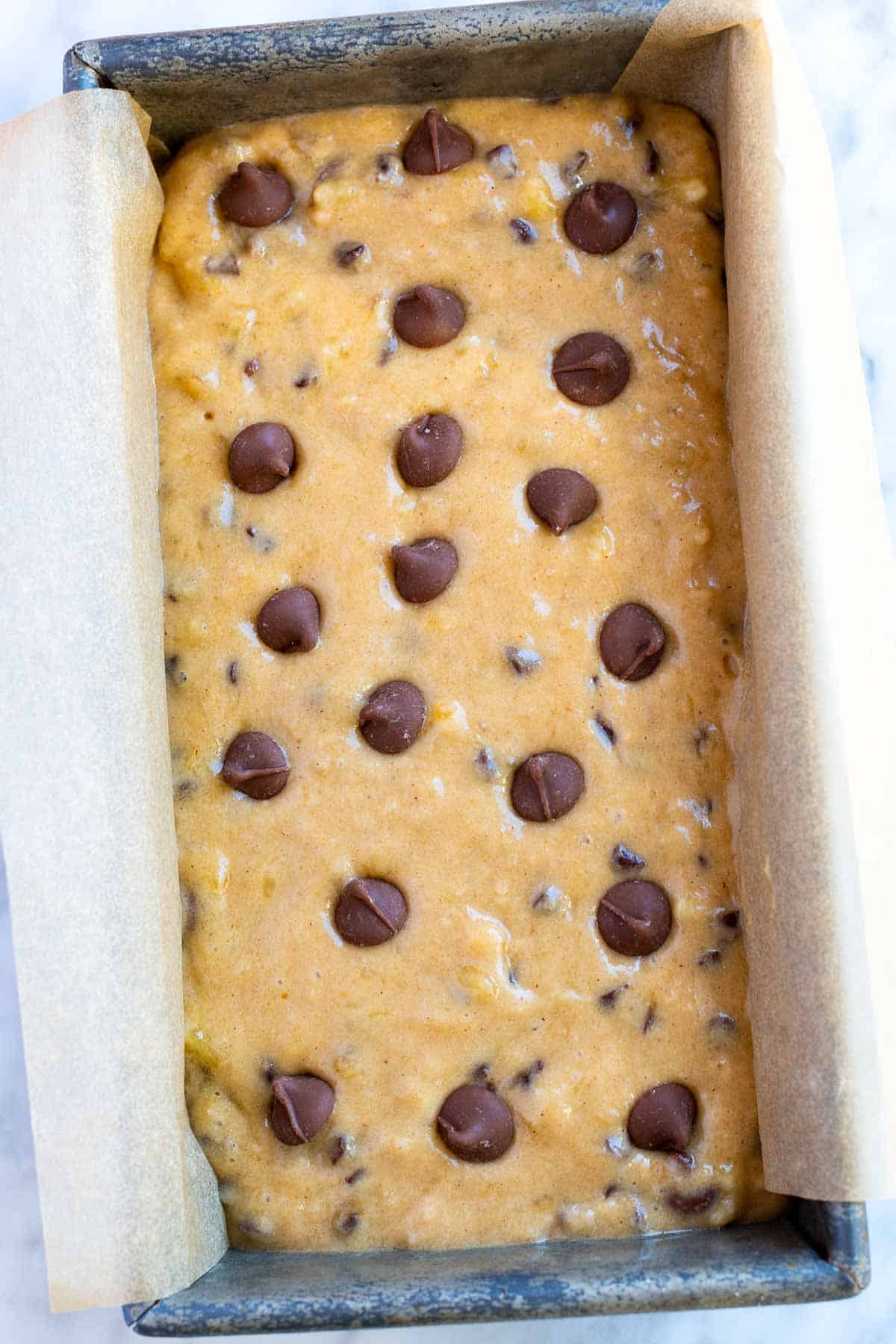 लोफ पैन में केले के ब्रेड बैटर के ऊपर कुछ अतिरिक्त चॉकलेट चिप्स डालें।