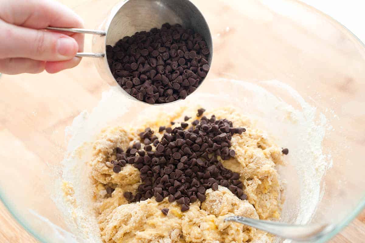 Mini chocolate chips being poured into a bowl with banana muffin batter.