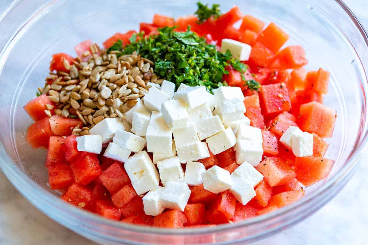 How to Make Watermelon Salad: ingredients in a bowl (watermelon, feta, fresh herbs, sunflower seeds, red wine vinegar, and olive oil)