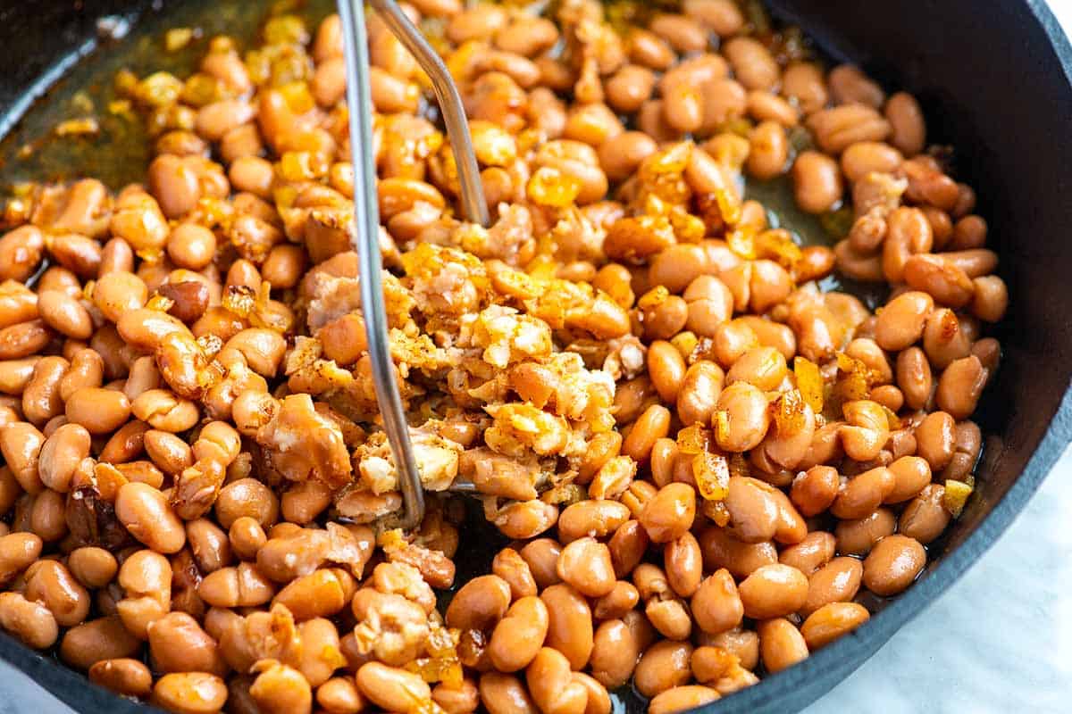 Mashing cooked beans into refried beans.