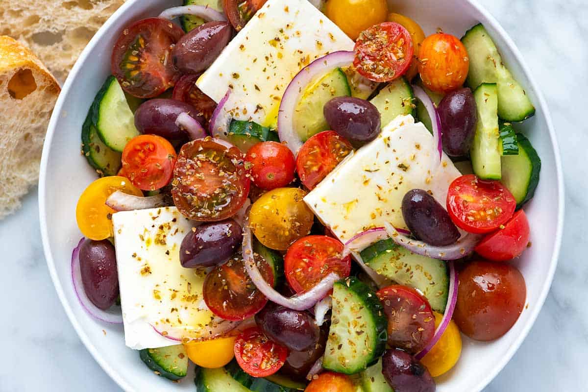 A bowl filled with a salad made of cucumbers, tomatoes, olives, red onion, and feta cheese. 
