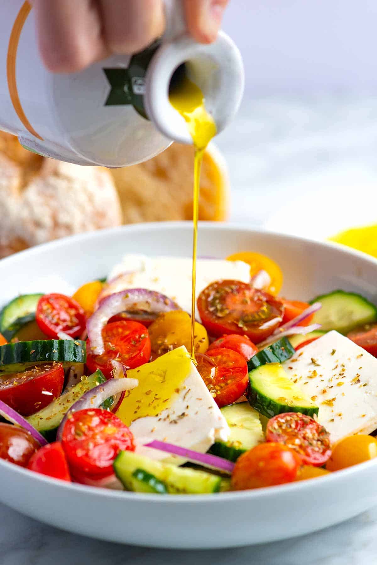 How to Make Greek Salad: Olive oil being poured over tomatoes, cucumber, feta, and onion