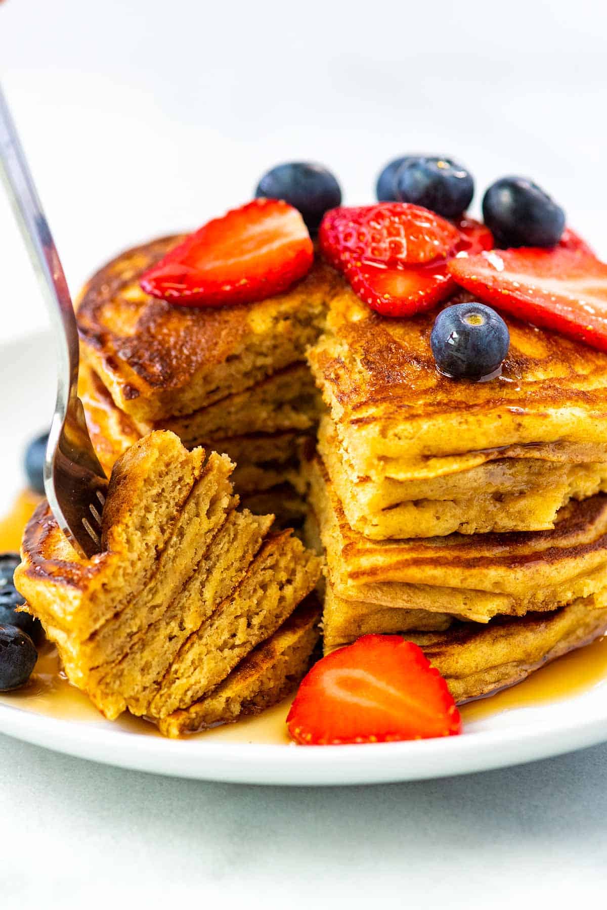 Stack of buttermilk pancakes with a fork, syrup and berries