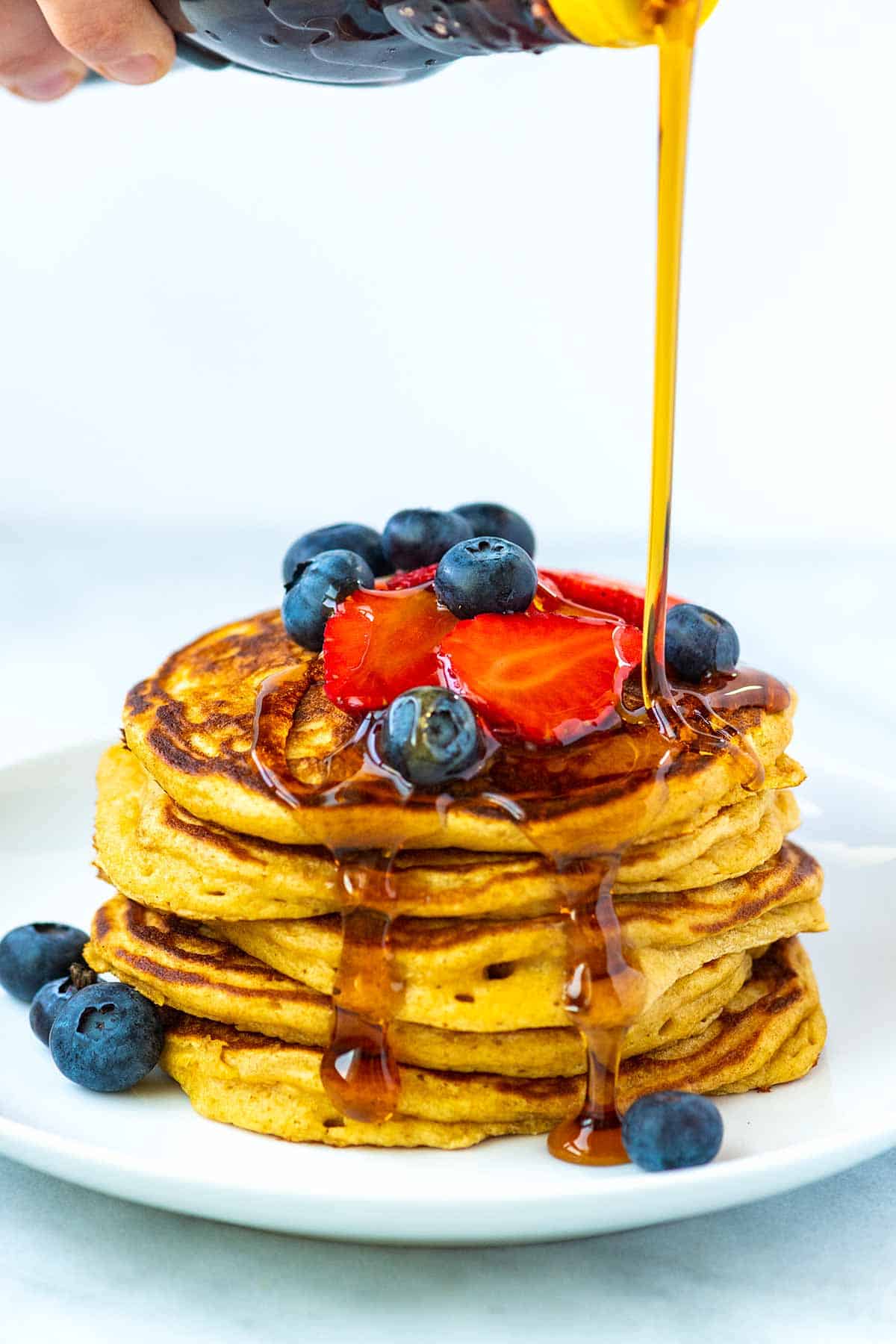 Drizzling maple syrup over a stack of buttermilk pancakes