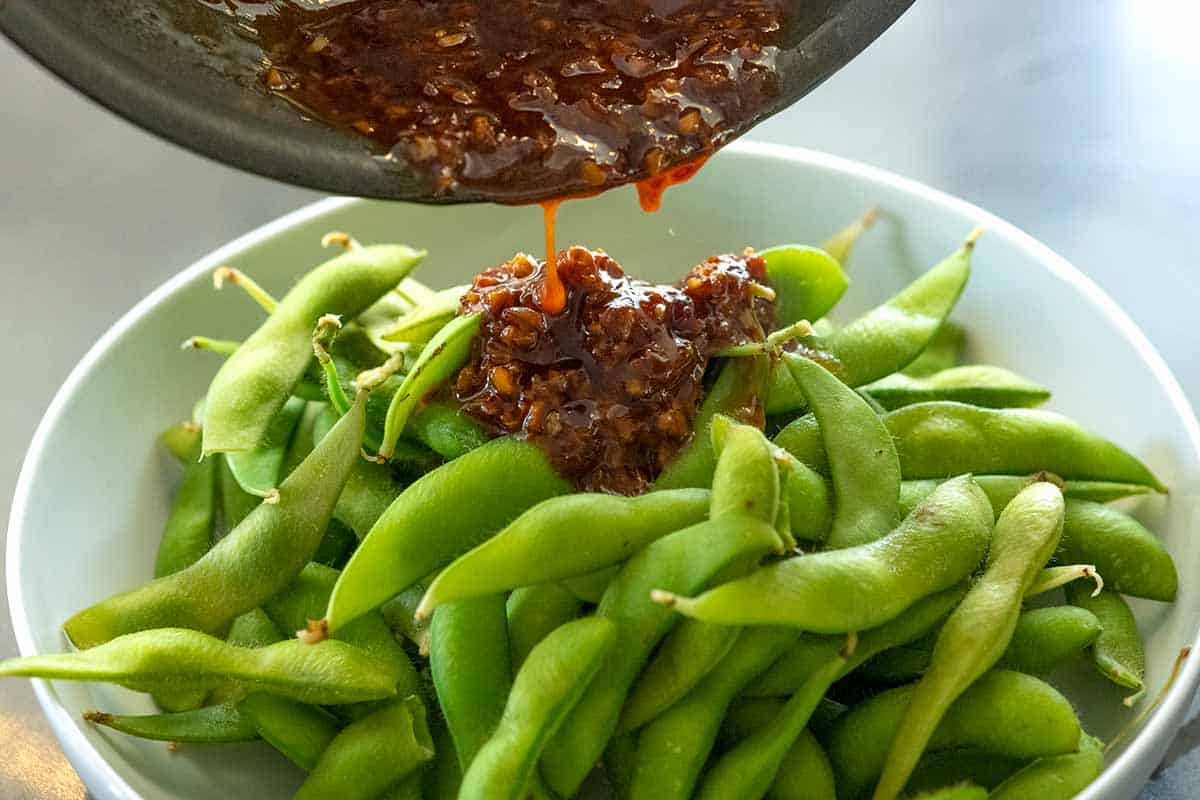 Tossing spicy garlic sauce with cooked edamame