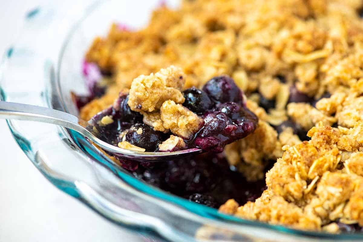 Scooping out blueberry crumble from a serving dish.