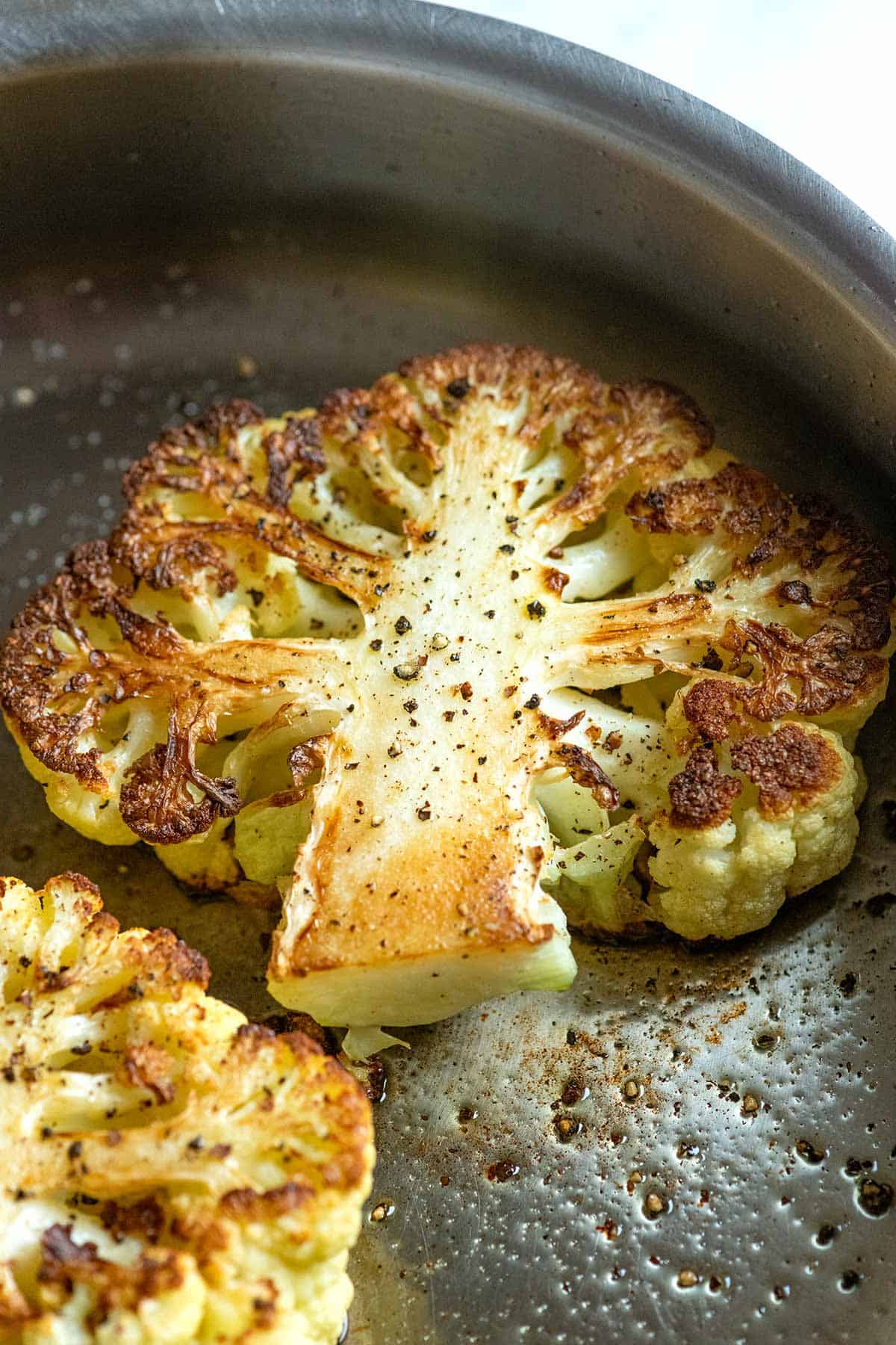 Step photo showing how to cook cauliflower steaks in a skillet. The cauliflower is golden brown and lightly seasoned with salt.