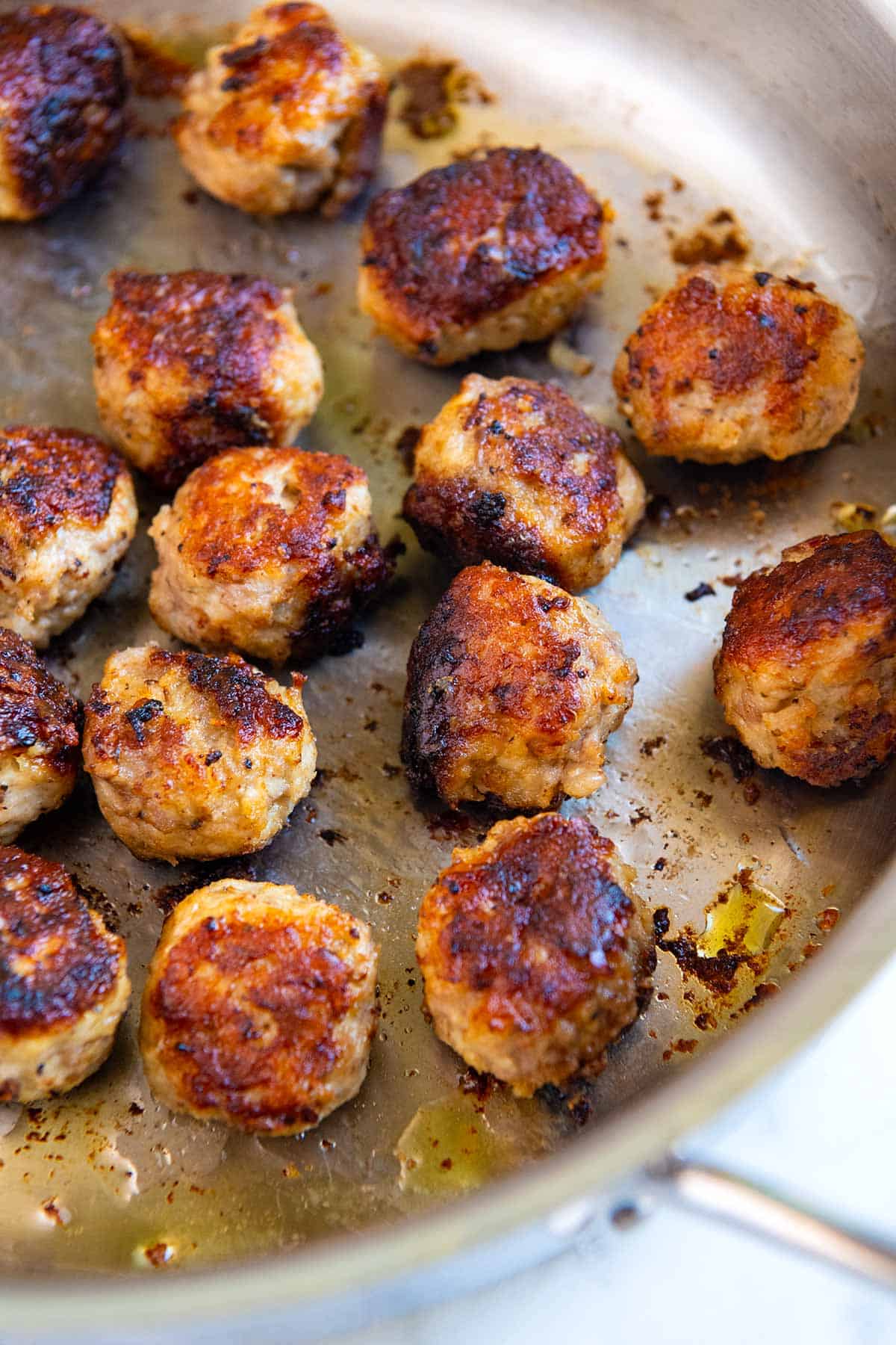 Step shot showing how to cook meatballs in a skillet.