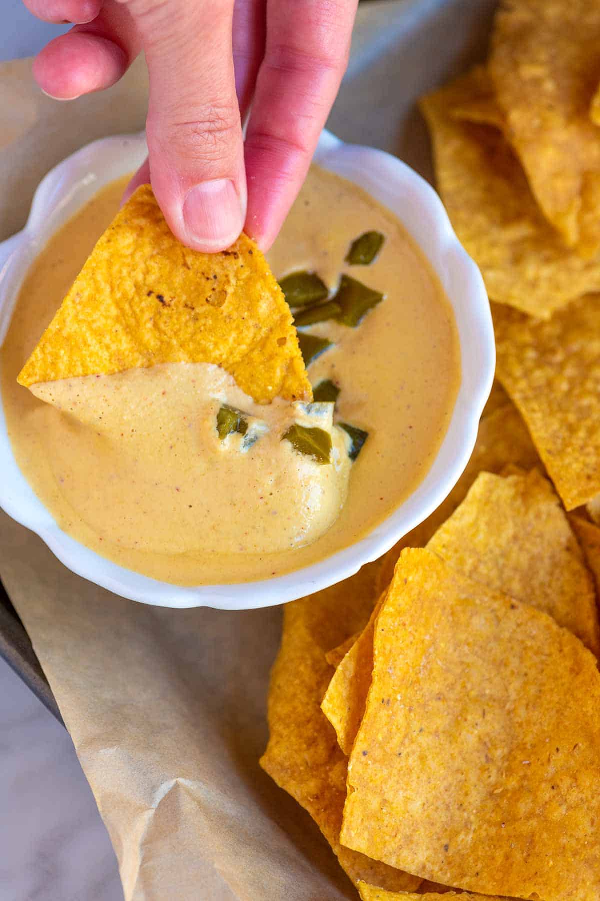 Dipping a tortilla chip into creamy vegan queso