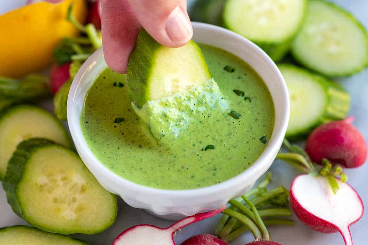 Dipping a cucumber into green goddess salad dressing