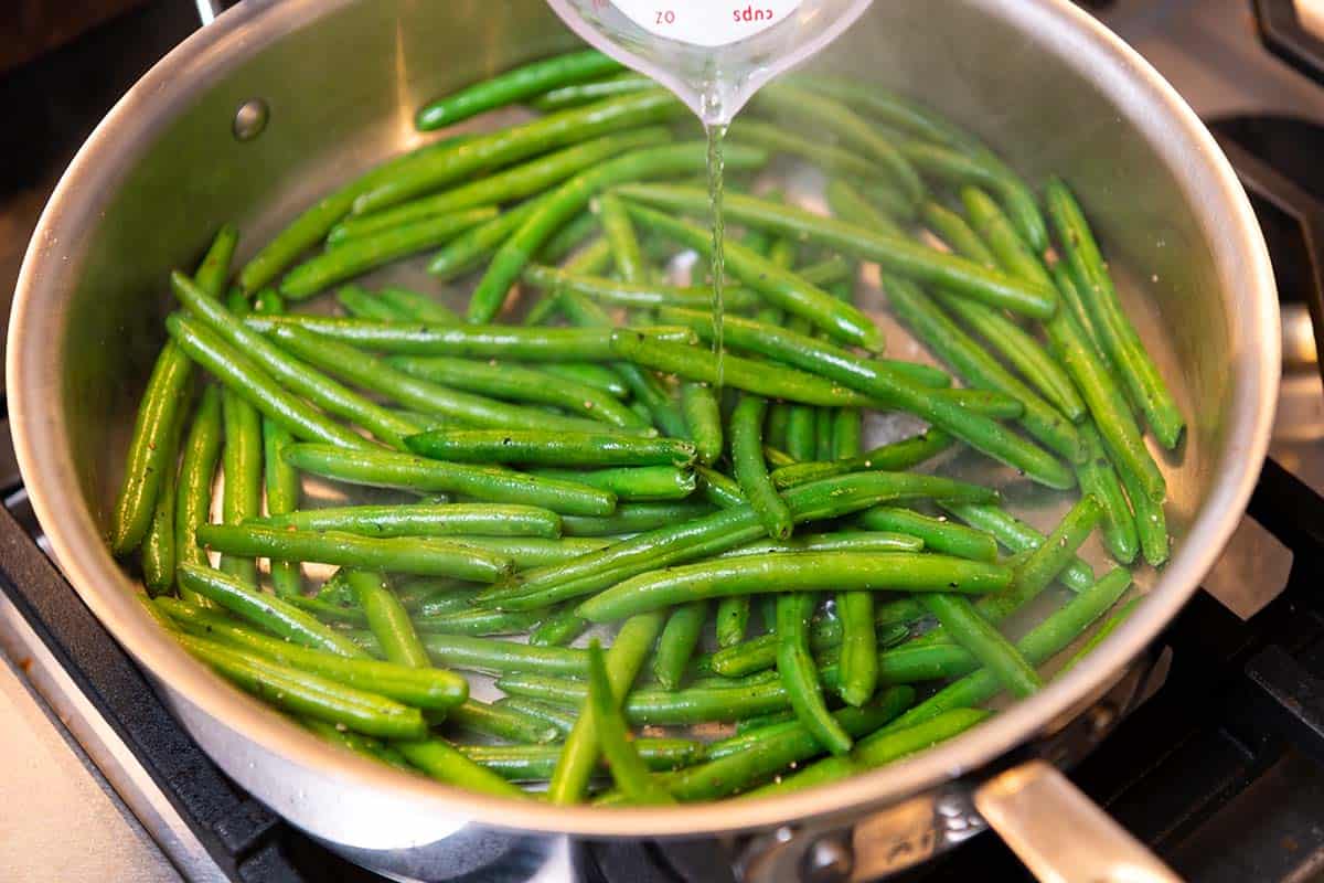 Adding liquid to fresh green beans cooking in a skillet