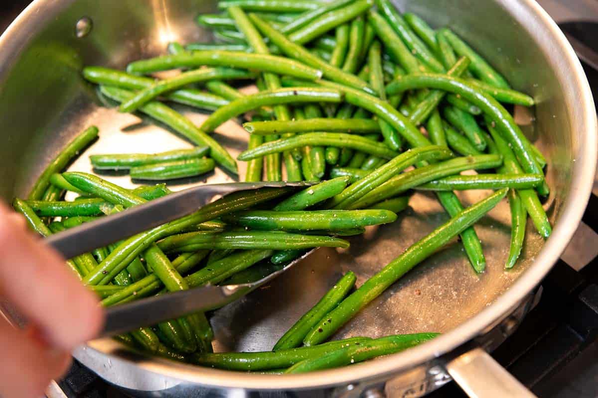 Sautéing fresh green beans in a skillet with oil