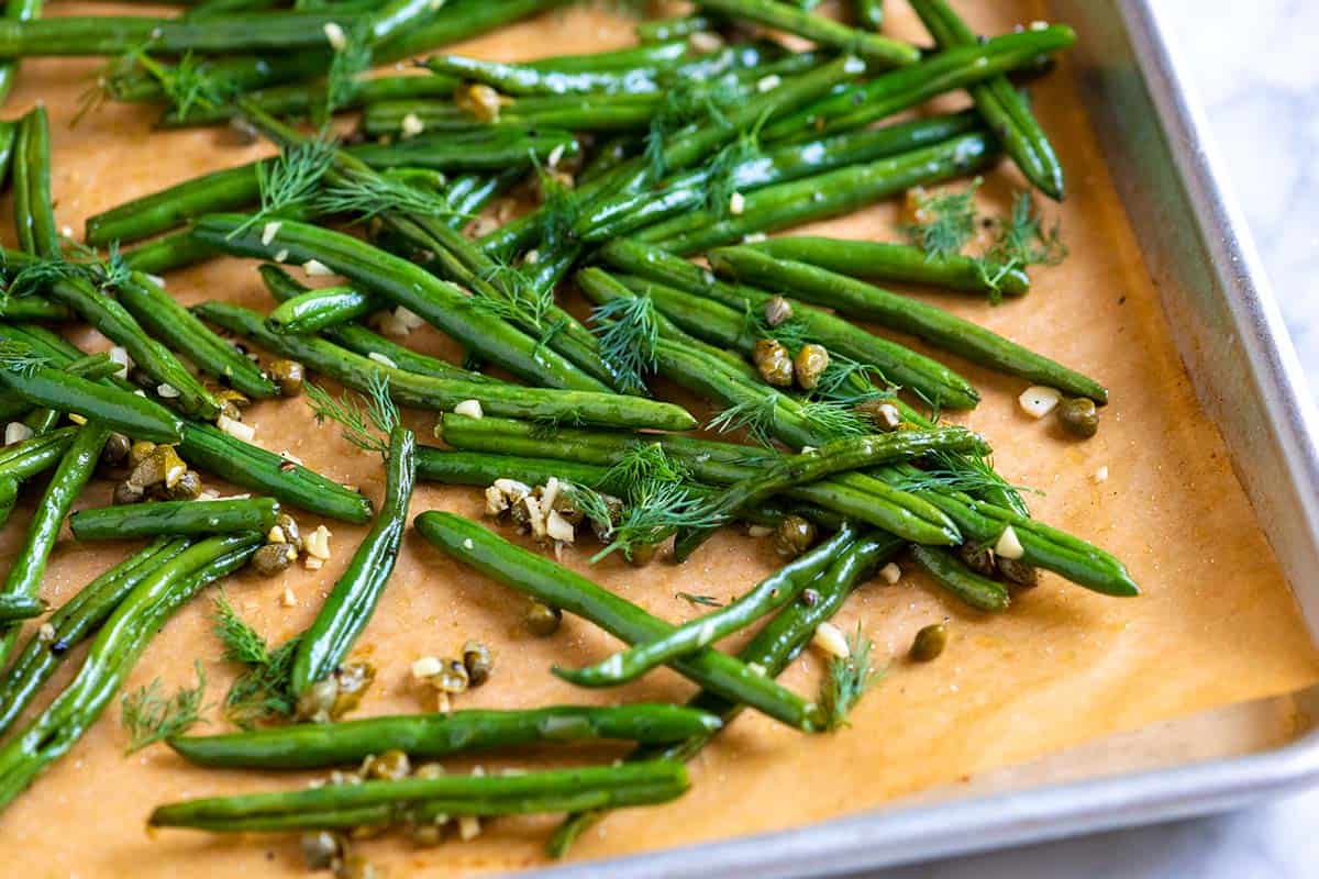 Perfect roasted green beans on a baking sheet with garlic, capers, and dill