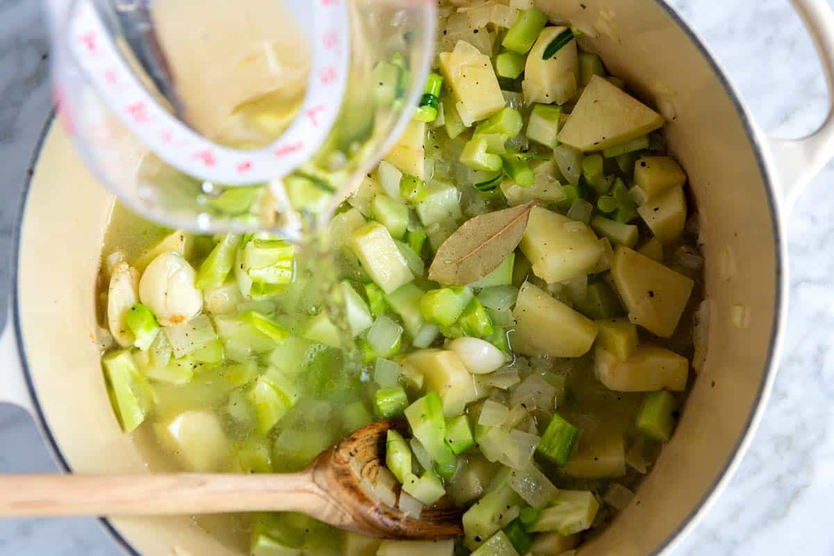 Adding water to the pot with potatoes, broccoli, and onions.