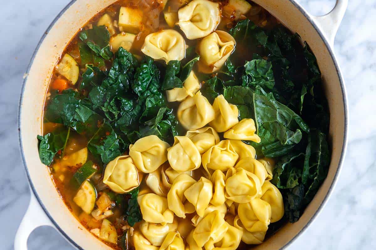 Adding tortellini and kale to the soup pot