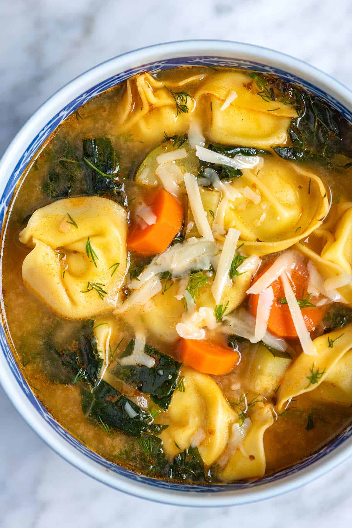 A bowl of tortellini soup with kale, carrots, and parmesan cheese