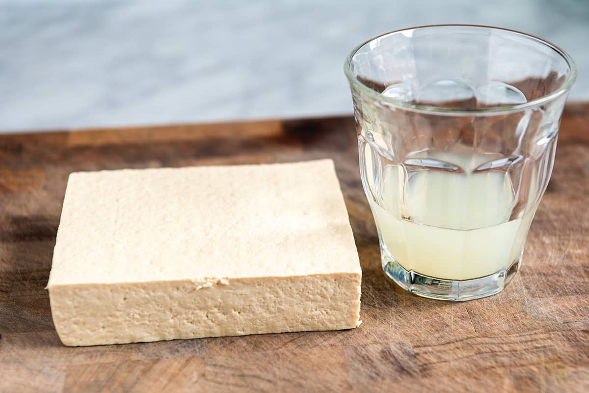 Tofu after pressing out the water next to a cup with water that's been pressed out.