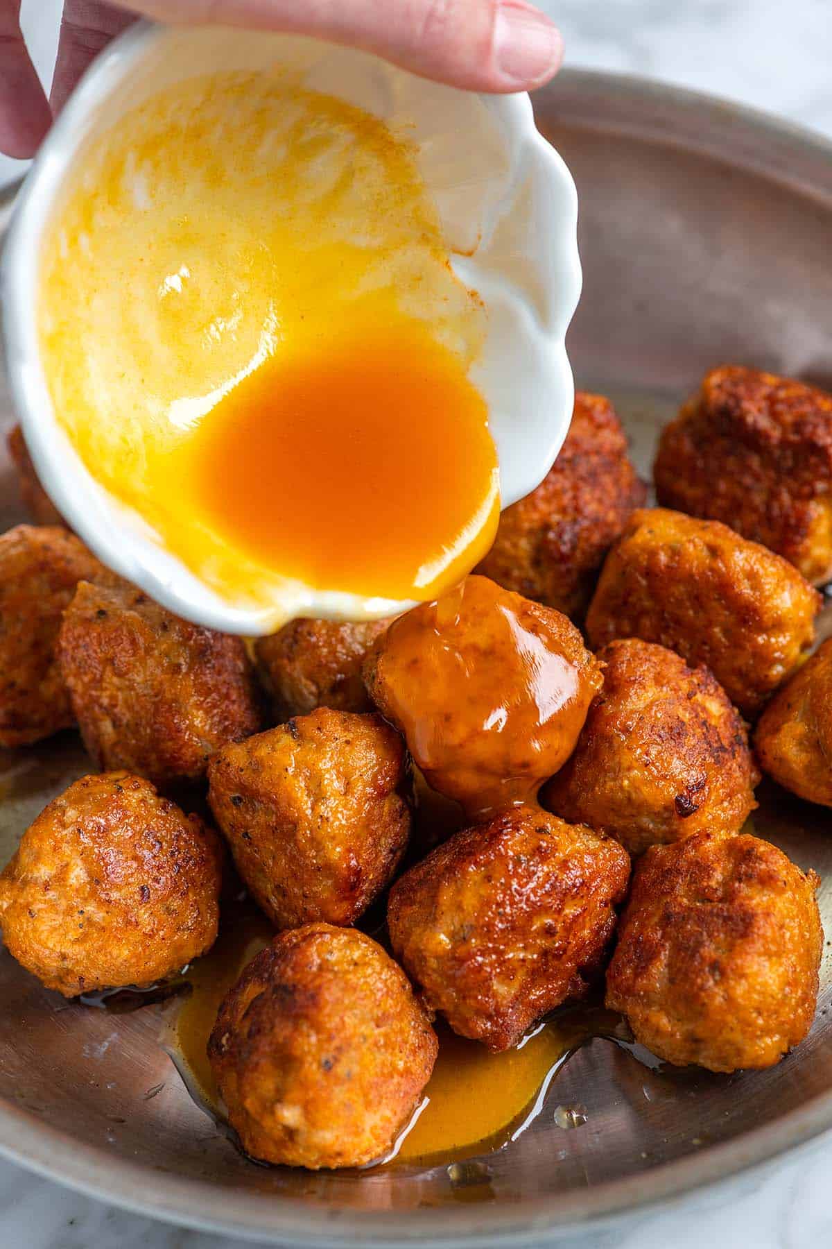 Pouring a sweet and spicy sauce of the chicken meatballs